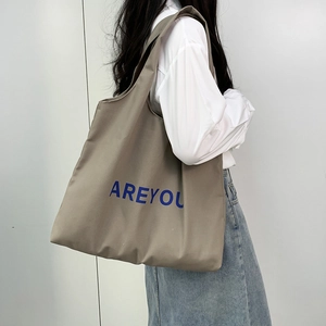Detailed view of khaki canvas tote bag with blue AREYOU print on a female model