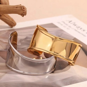 Polished 18K gold and silver wide wave bangles on a magazine background