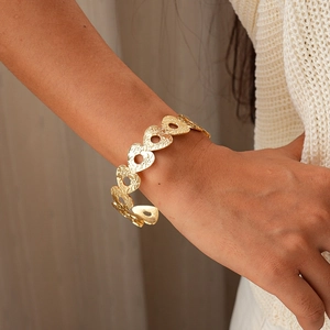Dettaglio di un bracciale a cuore dorato martellato indossato in uno stile minimalista