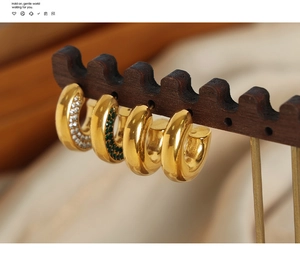 Close-up of gold C-shaped hoop earrings with white and green stones on a wooden stand