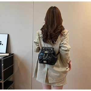 Rear view of a black quilted leather mini backpack with gold chain straps on a model