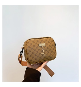 Close-up of vintage brown monogram square bag featuring a gold deer pendant and wide strap