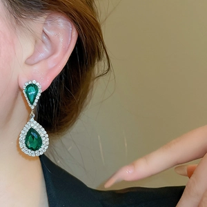 Close-up of sparkling waterdrop emerald earrings with diamond-set halo for luxury look