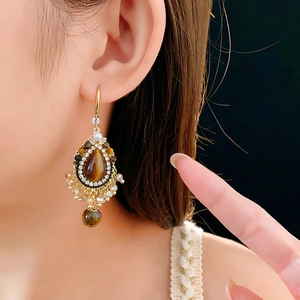 Close-up of vintage gold earrings with tiger eye stone and pearls worn by a model