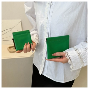 Macro detail of two green mini leather pouches with metal snap closures held by a person