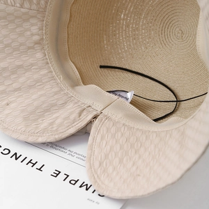 Detail of light beige straw sun hat showing interior texture, chin strap and label