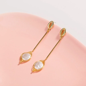 Golden seashell drop earrings with wire-wrapped white pearls on a soft pink ceramic plate