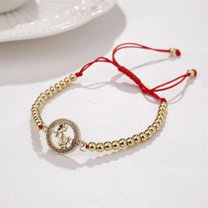 Détail du bracelet cordon rouge avec perles dorées et lettrage MAMA avec zircon