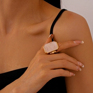 Detail view of a chunky gold ring featuring a large rectangular translucent pink gemstone