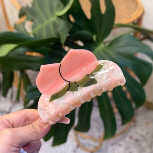 Macro detail of peach-shaped acetate hair claw with pink marble texture and green leaves
