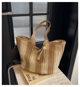 Detailed close-up of striped straw tote bag with woven handles and beaded tassel charm