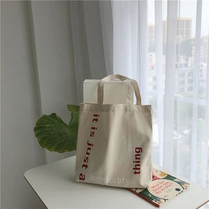 Close-up of beige canvas tote bag with red artistic lettering in a minimalist setting