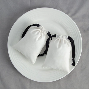 Detail view of two white cotton jewelry pouches with black satin drawstrings on a plate