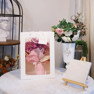 Detail of white gift bag with transparent window featuring pink floral bouquet and card