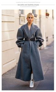 Detail of a wide black waist belt with a gold square buckle on a grey cashmere coat