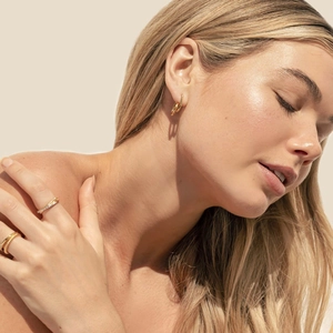 Detail of 18K gold double-hoop earring and stacking rings on model for a trendy look