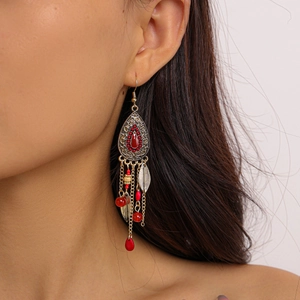 Detail of vintage drop earrings with red gems and metallic tassel pendants on model