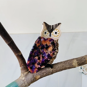 Detailed close-up of a vibrant owl-shaped acetate hair clip perched on a tree branch