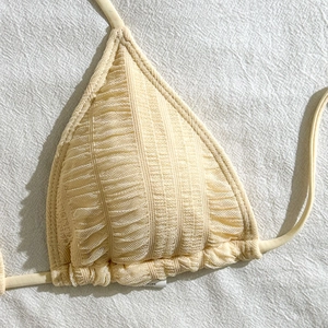 Detailed close-up of beige ruched mesh fabric texture on a triangle bikini top cup