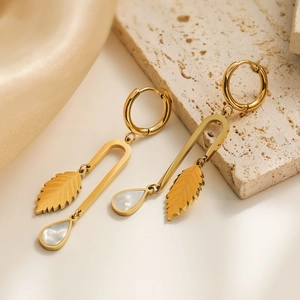 Gold leaf earrings with shell drops displayed on elegant silk and stone background