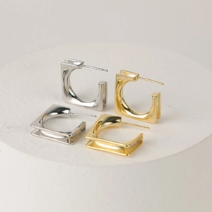 Detail view of gold and silver square C-shaped earrings with minimalist groove design