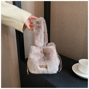 Detail of light brown plush bucket bag with drawstring closure and engraved metal tag