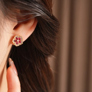 Macro shot of gold floral earrings with red gemstones and white zircons on ear