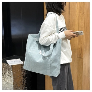 Detail of light blue corduroy tote bag with side shoulder strap and white woven label
