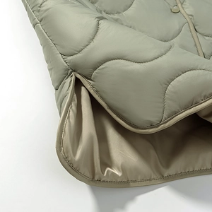 Detailed view of wave-quilted hem and side slit on a green padded cotton jacket