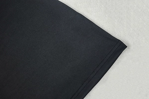 Detailed view of the clean-finished hemline and textured black fabric of the mini dress