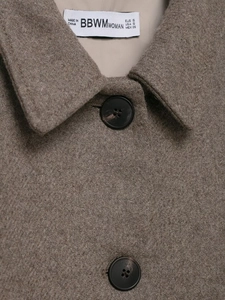 Detailaufnahme des Revers eines Wollmantels mit schwarzem Knopf und Stoffstruktur