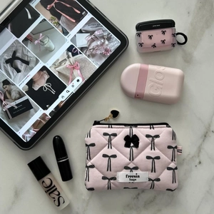 Flat lay of pink quilted makeup bag and bow headphone case on marble surface