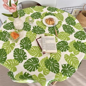 Detail of round cotton linen tablecloth with green monstera leaf print in a cozy setting