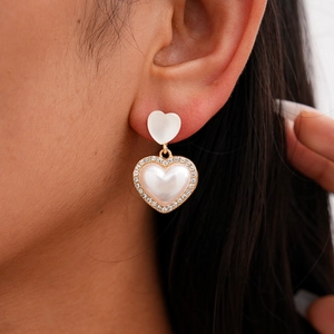 Close-up of double heart earrings with pearl centers and rhinestone pavé in gold