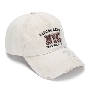 Close-up of NYC embroidery and distressed frayed edges on the beige denim baseball cap