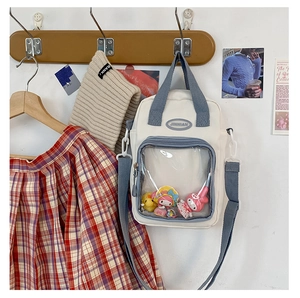 Close-up of beige canvas ita bag featuring a large clear PVC window and blue handles