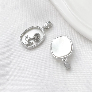 Detail of silver rose pendant and square white shell charm on textured white fabric