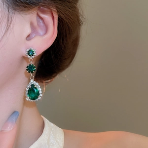 Detail of vintage style earrings with green teardrop emeralds and dangling diamond tassels