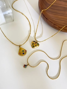 Close-up of golden necklaces with shell, heart, and flower pendants with colorful crystals