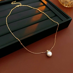 Detailed close-up of gold beaded chain with a glossy white faux pearl on jewelry display