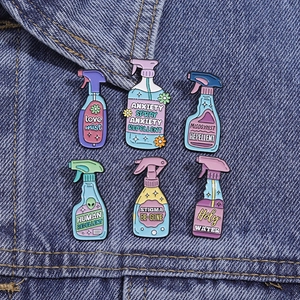 Close-up of colorful spray bottle enamel pins on denim, featuring creative themes