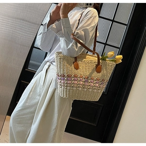 Detail of a large woven straw tote bag with brown leather straps and floral accents