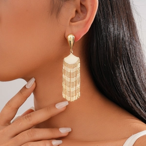 Macro detail of elegant golden fan-shaped tassel earrings worn by a fashion model