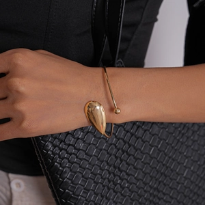 Detail of a polished gold teardrop open bangle showing high-gloss mirror finish metal texture