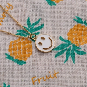 Macro shot of gold plated necklace featuring a white enamel smiley face pendant