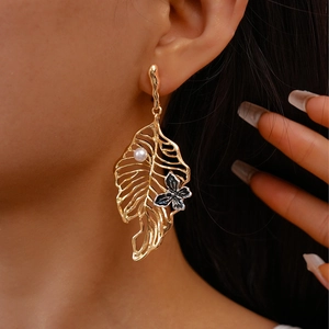 Golden hollow leaf earrings with white pearl and black butterfly detail on model