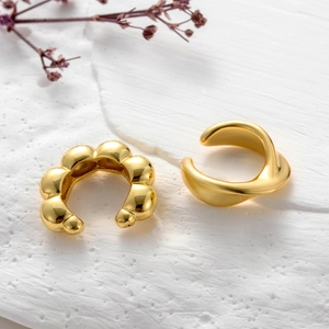 Detail of gold bubble and wavy ear cuff set on minimalist textured surface