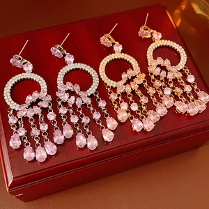 Macro detail of gold and silver drop earrings with pink crystals on dark wooden box