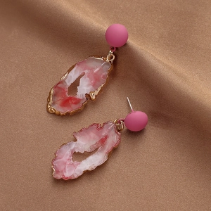 Detail of pink resin earrings with faux agate slices on brown textured fabric background