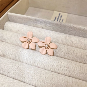 Detailed macro view of pink matte flower earrings with a small pearl center on beige velvet